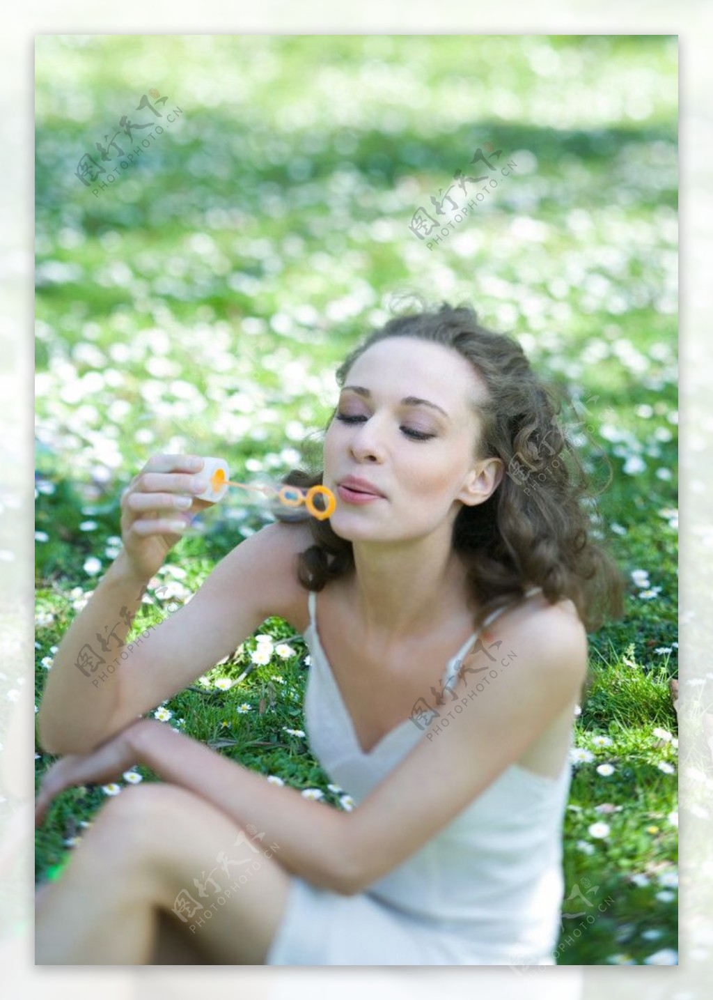 坐在绿草地上吹泡泡的快乐美女图片